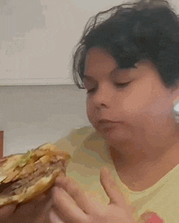 a woman is eating a hamburger in a kitchen .