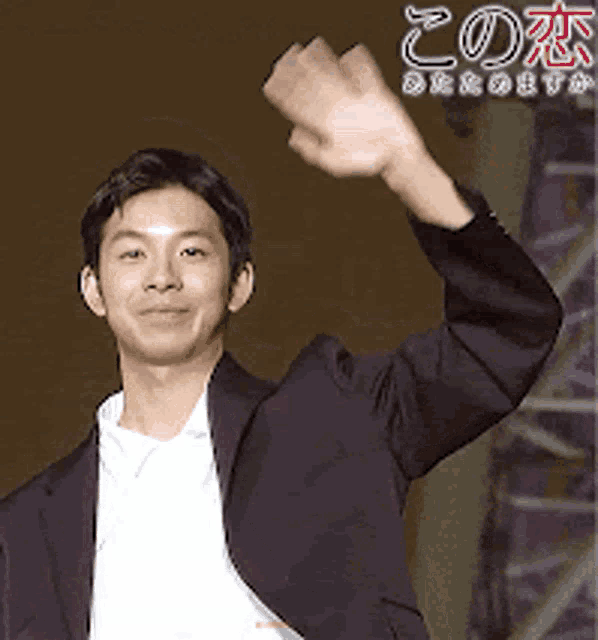 a man in a suit and white shirt is waving his hand in the air .