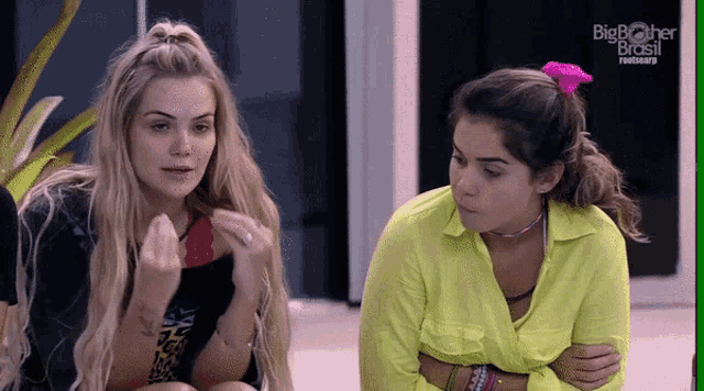 two blonde women are sitting next to each other with big brother brasil written on the screen behind them