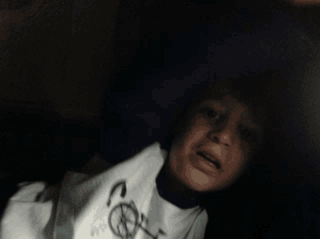 a young boy wearing a white shirt with a peace sign on it looks at the camera