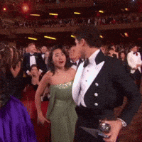 a man in a tuxedo holds a trophy in front of a woman in a green dress
