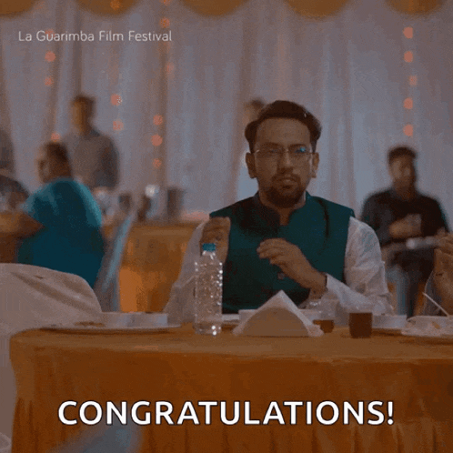 a man sitting at a table with a congratulations sign
