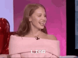 a woman is sitting in a chair and laughing with the word liar written on the screen behind her .