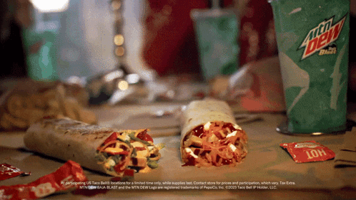 two burritos are on a table next to a mountain dew cup