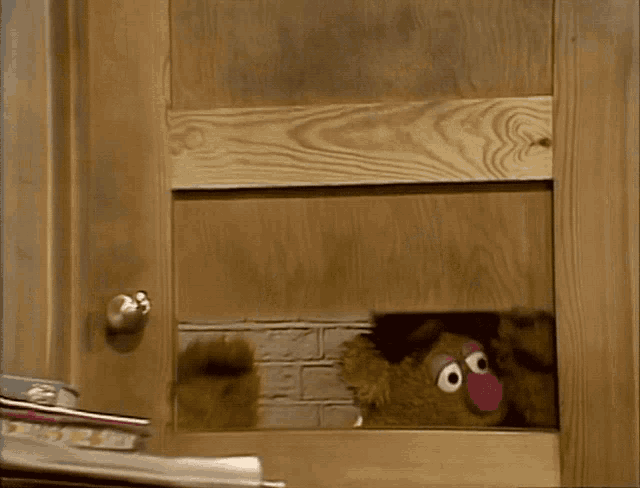 a teddy bear wearing a top hat looks out of a wooden window