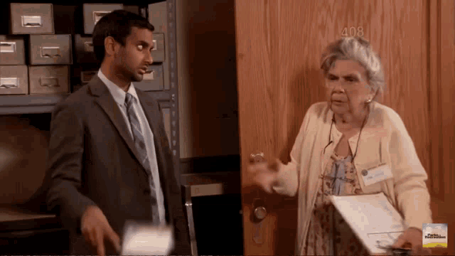 a man in a suit and tie stands next to an elderly woman in front of a wooden door that says 408