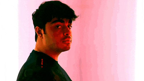 a man in a black shirt is standing in front of a pink wall and looking to the side .