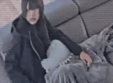 a person in a black jacket is sitting on a couch with a blanket .
