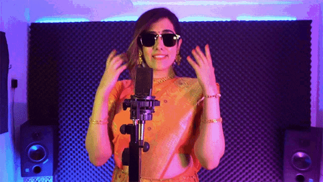 a woman wearing sunglasses and an orange top is standing in front of a microphone
