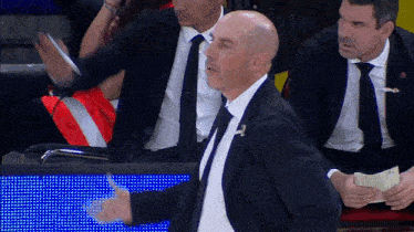 a bald man in a suit and tie stands in front of a crowd