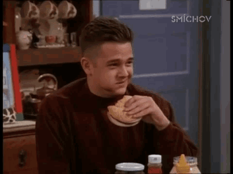 a man is eating a sandwich in front of a blue door with smichov on the bottom right