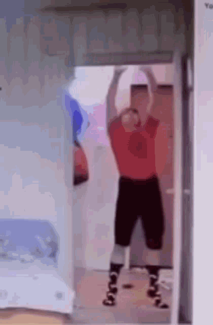 a man in a red shirt and black shorts is standing in a doorway .