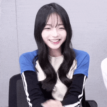 a girl with long hair and bangs is smiling and wearing a blue and white shirt