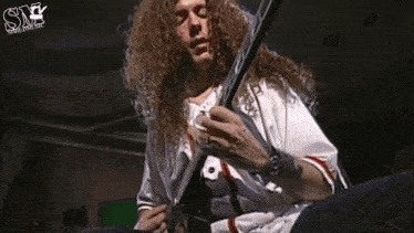 a man with long curly hair is playing a guitar in front of a sign that says sn