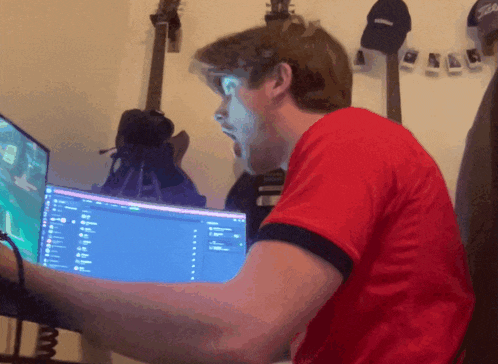 a man in a red shirt is sitting in front of a computer monitor
