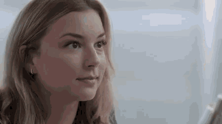a close up of a woman 's face looking at the camera while sitting in front of a window .