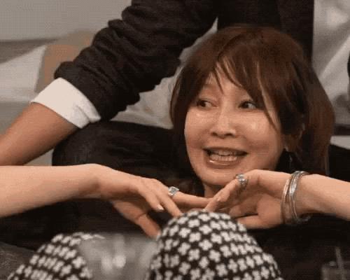 a woman is making a heart shape with her hands and smiling while sitting on a couch .