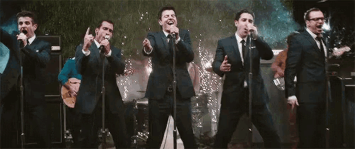 a group of men in suits and ties are singing into microphones on a stage .