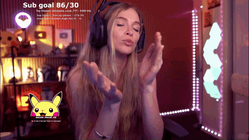 a woman wearing headphones blows a kiss in front of a screen that says ' sub goal 86/30 ' on it