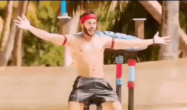 a shirtless man with his arms outstretched is standing on a pole .
