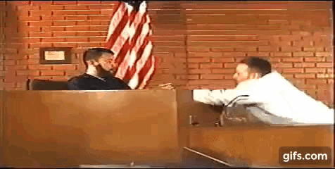two men are sitting in front of a brick wall in a courtroom talking to each other .