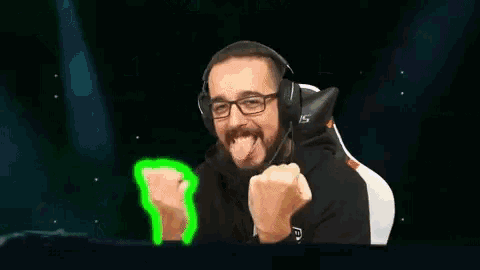 a man with a beard and glasses is wearing headphones and sticking out his tongue .