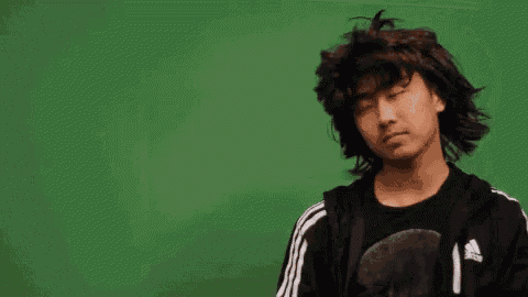 a young man with long curly hair is standing in front of a green screen with his eyes closed .