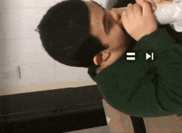 a man in a green sweater is playing a video with the letters b and i on the bottom of the screen