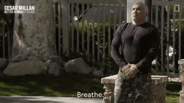 a man in a purple shirt stands in front of a fence with the caption breathe