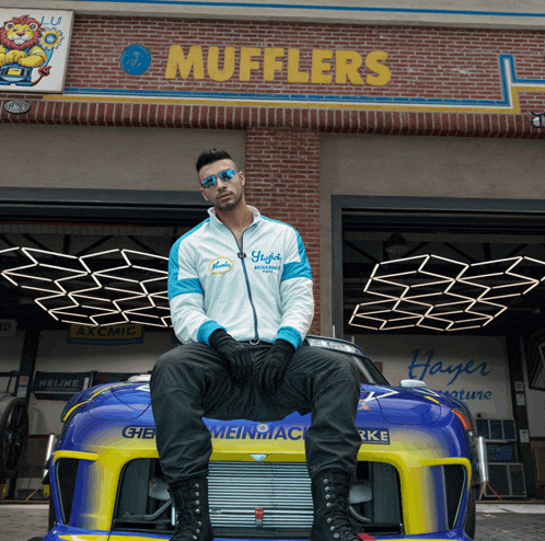 a man sits on the front of a race car in front of a building that says mufflers