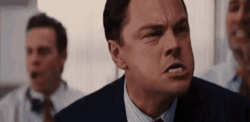 a man in a suit and tie is making a funny face in front of a group of men .