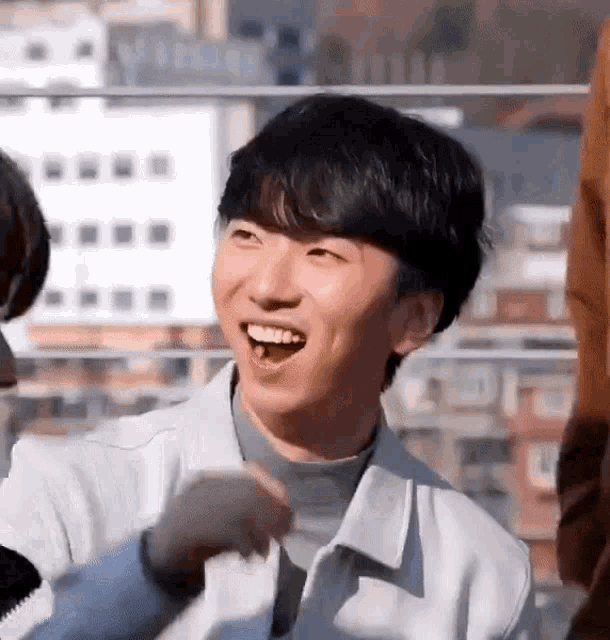 a young man in a white jacket is smiling and laughing while standing in front of a group of people .