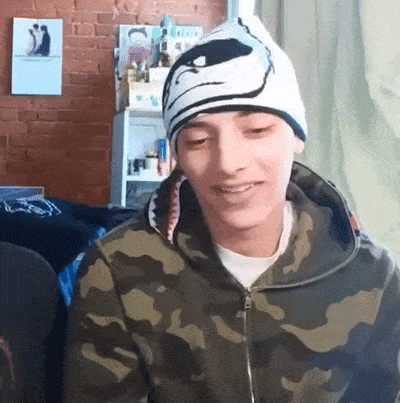a young man wearing a camouflage jacket and a beanie with a shark on it