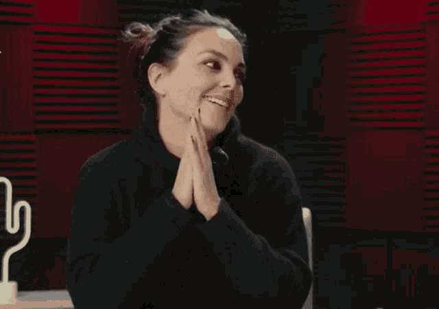 a woman in a black sweater is sitting at a table with her hands folded in front of her face .