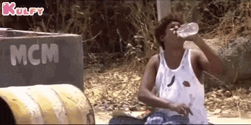 a man in a white tank top is drinking water from a bottle .