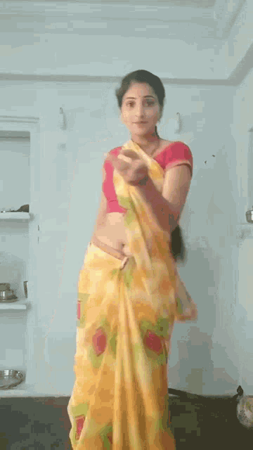 a woman wearing a yellow saree and a red blouse is standing in a room .
