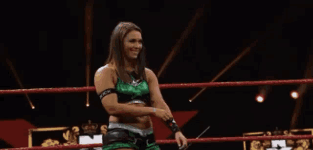 a woman in a green outfit is standing in a wrestling ring holding a microphone