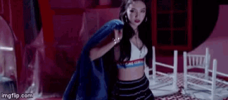 a woman in a crop top and skirt is holding a blue jacket over her shoulder in a room .