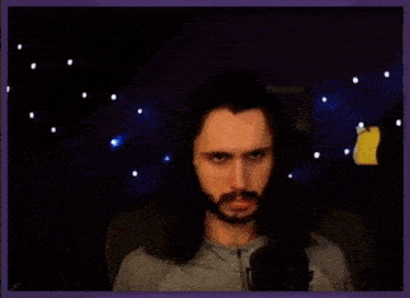 a man with long hair and a mustache is making a funny face while sitting in front of a microphone .