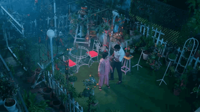 a man and a woman are standing in a garden surrounded by plants
