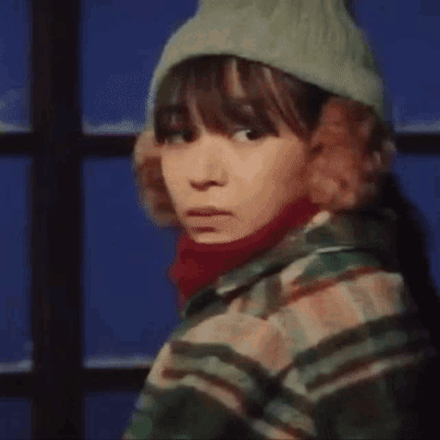 a woman wearing a hat and scarf is looking at the camera .