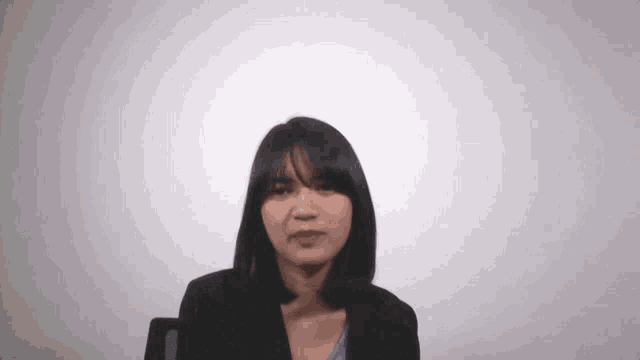 the woman is wearing a black jacket and a purple shirt and making a funny face .