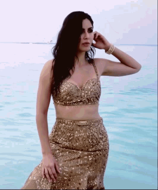 a woman in a gold dress is standing in the ocean