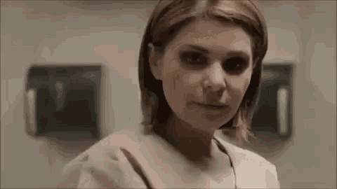a woman in a hospital gown with black eyes is looking at the camera in a bathroom .