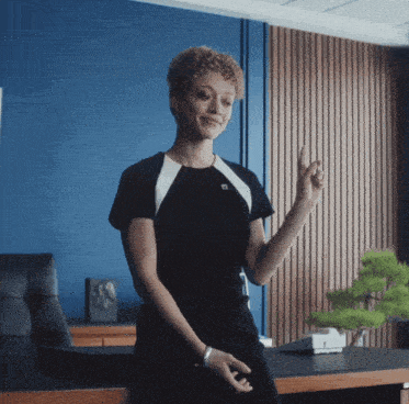 a woman in a black and white dress is sitting at a desk giving a peace sign