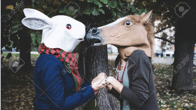 a woman wearing a rabbit mask and a horse mask holds hands with another woman
