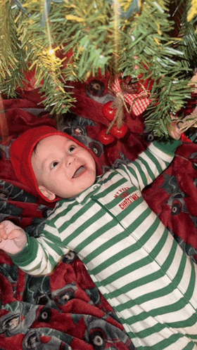 a baby laying under a christmas tree wearing a green and white striped outfit