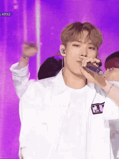 a young man in a white jacket is singing into a microphone on stage .