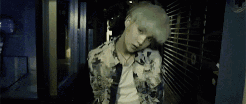 a young man with green hair is standing in a dark alleyway looking at the camera .