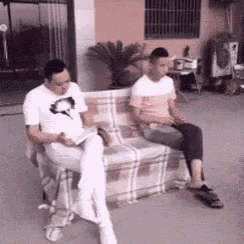 two men are sitting on a couch reading books and talking .